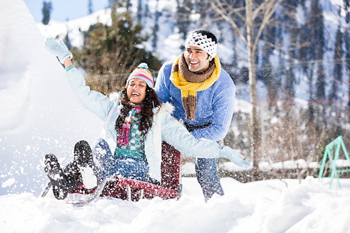 Couple enjoying snow sledding in Mussoorie during winter trip.